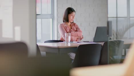 Focused-asian-businesswoman-looking-at-laptop-at-table-in-empty-meeting-room,-in-slow-motion