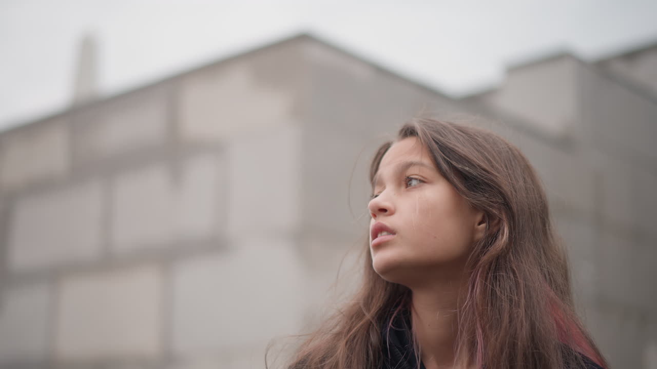 Menina para silenciosamente ao lado de poças cheias de chuva. Jovem mulher parada perto da parede com cabelo molhado em humor contemplativo. Figura feminina para sozinha em calçada chuvosa em estado de espírito reflexivo e sombrio
