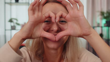 happy girl makes symbol of love, showing heart sign to camera, express romantic feelings, charity