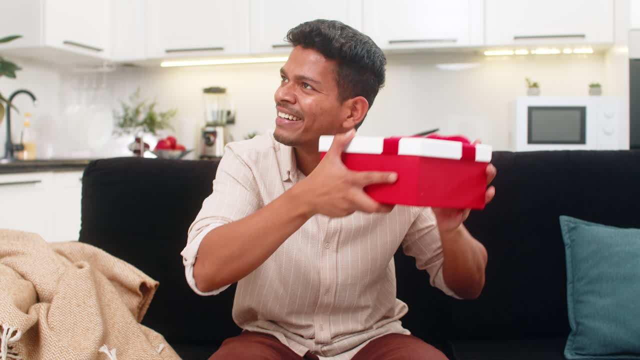 Indian man shakes gift box listens guesses content playful smile tries to predict present with fun