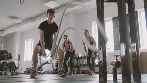 an athletic young man works with battling ropes while gym buddies support him