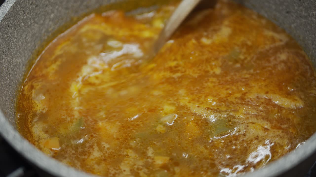 cocinar sopa en una sartén de piedra de cerca - agitando con una cuchara de madera en cámara lenta