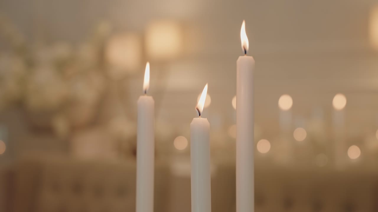 three lit white candles flicker gently in soft indoor atmosphere
