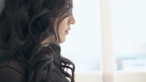 young woman with dark hair poses at window close side view