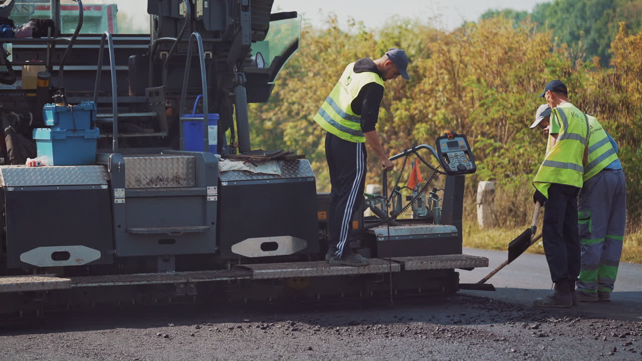 Team of workers and asphalt machine outdoors in autumn. Men workers in special clothing work on the road during asphalting.