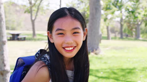 slow motion portrait of young girl with backpack in park smiling at camera