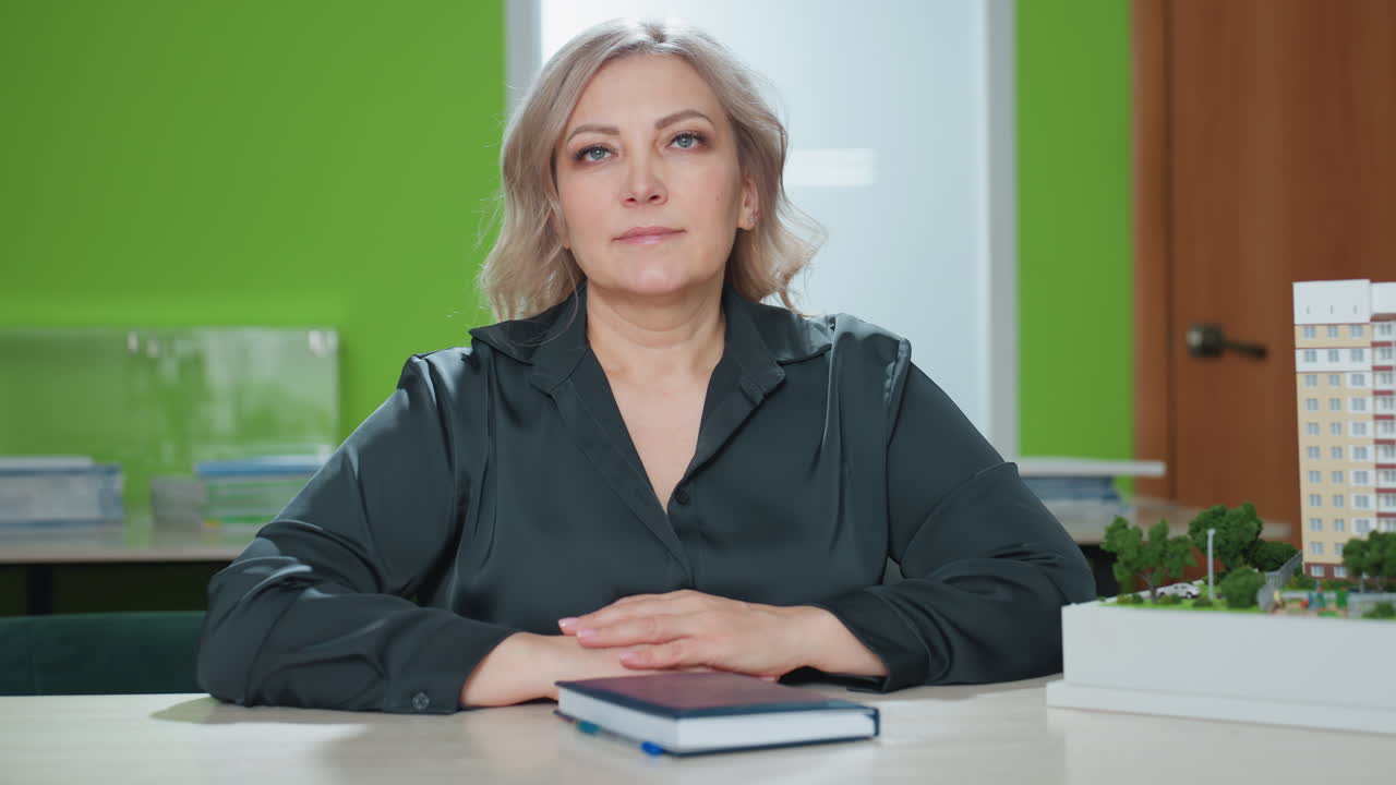 real estate agent closes book and gently places hand on cover next to architectural building model on modern office desk in bright workspace, exuding professionalism and calm composure