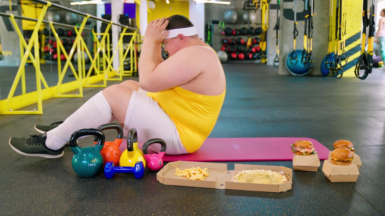 Uomo in sovrappeso che fatica con gli addominali mentre è circondato da fast food in palestra
