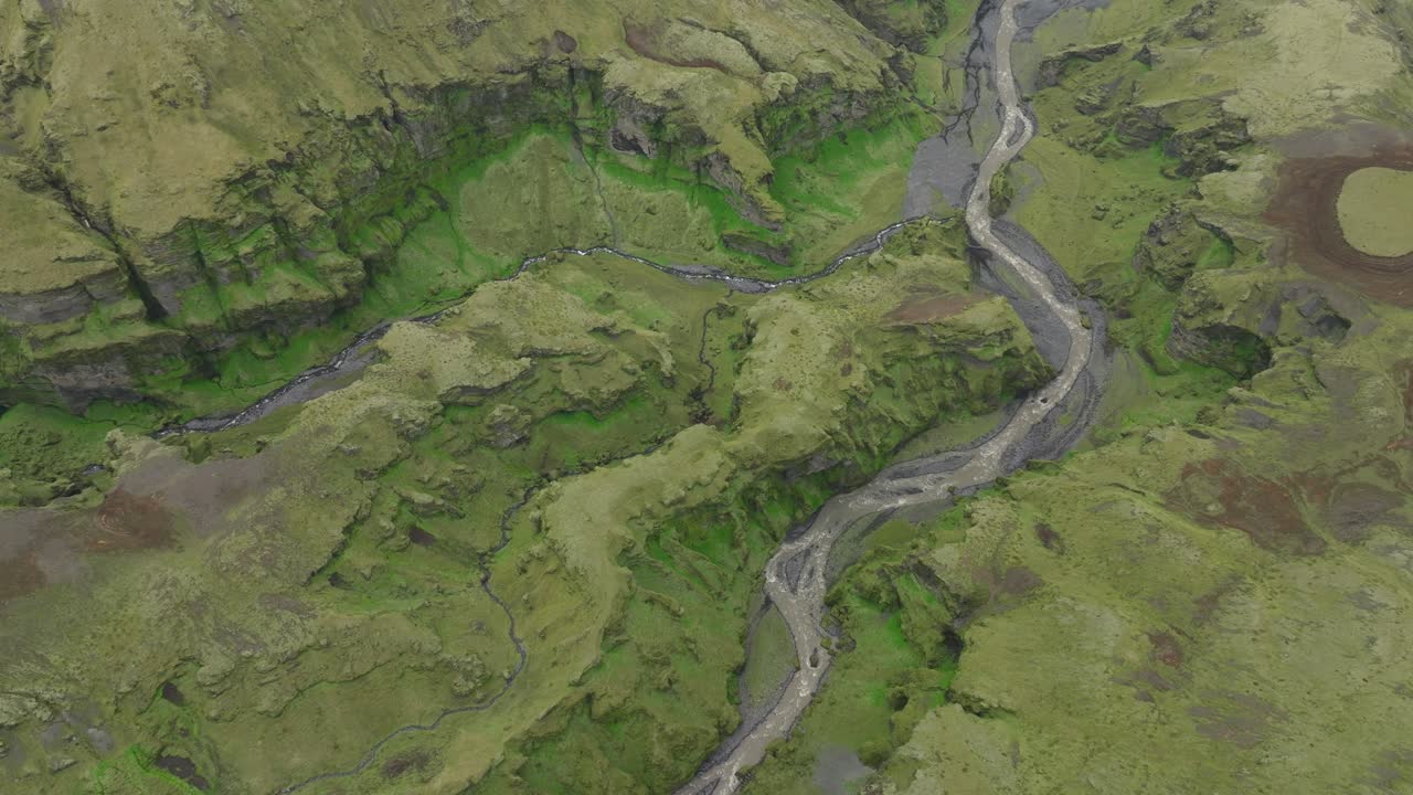 A stunning aerial view of a winding river cutting through a green valley in Hafursey, Iceland, surrounded by rugged cliffs and lush terrain.