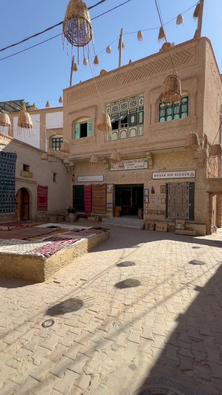 Cortile soleggiato nel centro storico di Tozeur con tappeti appesi, lampade intrecciate e la facciata di un negozio di tappeti, Tunisia.