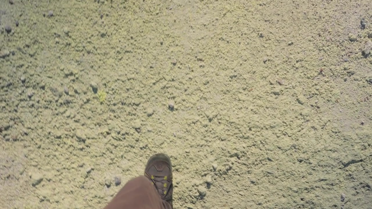 Punto di vista di una persona che indossa scarpe da trekking e cammina su terreno solforoso giallo, esplorando il paesaggio geotermico del Parco Nazionale di Akan Mashu a Hokkaido, Giappone. Scatto dall'alto in stile UGC.