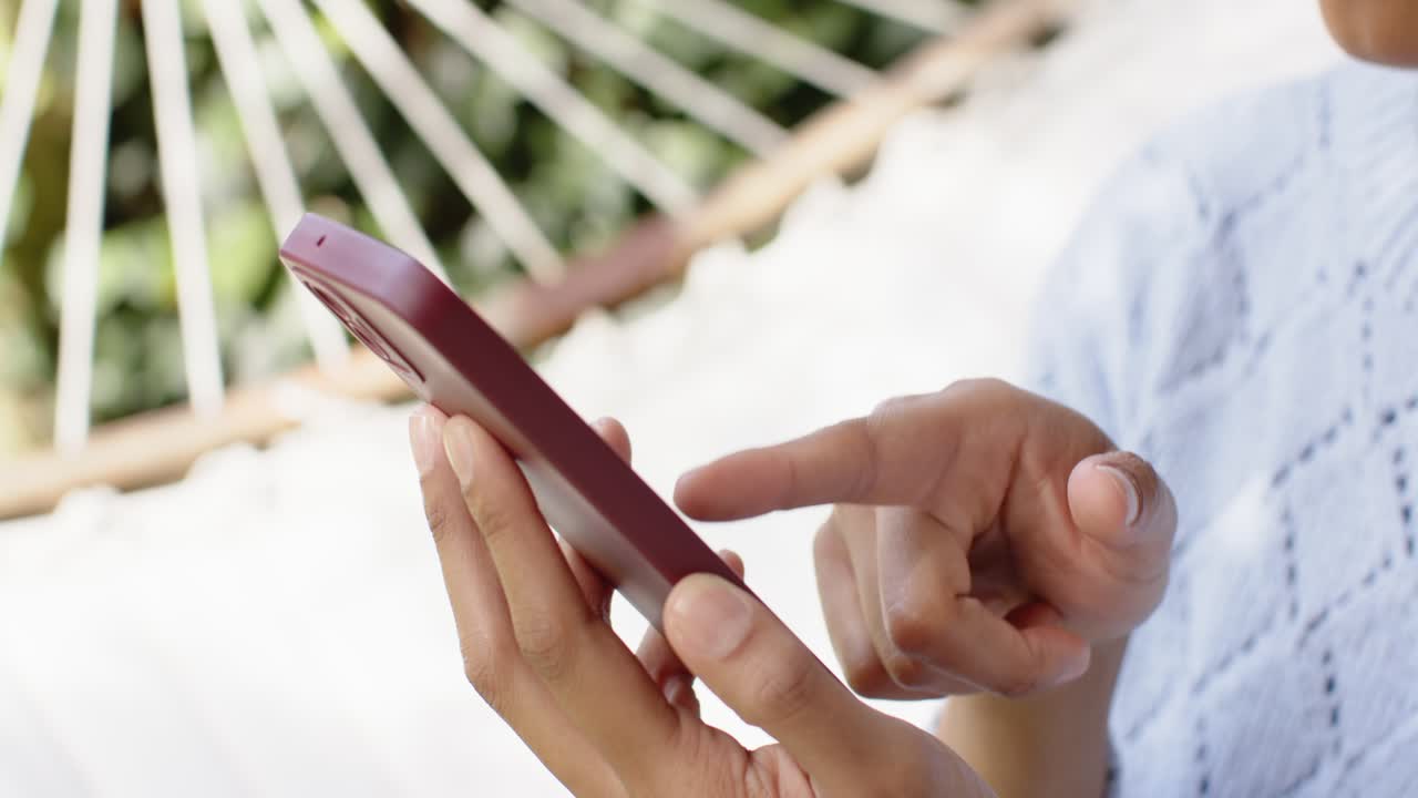 Woman's hands are tapping to wake maroon phone, swiping and confirming selection in hammock garden