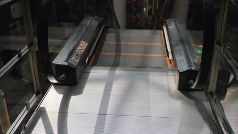 una vista detallada de una escalera mecánica que desciende en un centro comercial, capturada desde una perspectiva en primera persona utilizando una cámara portátil. la escena destaca la mecánica de la escalera mecánica