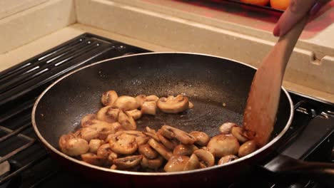 close up of woman stirring sliced button mushrooms to saute in butter in a skillet in a tiny home kitchen