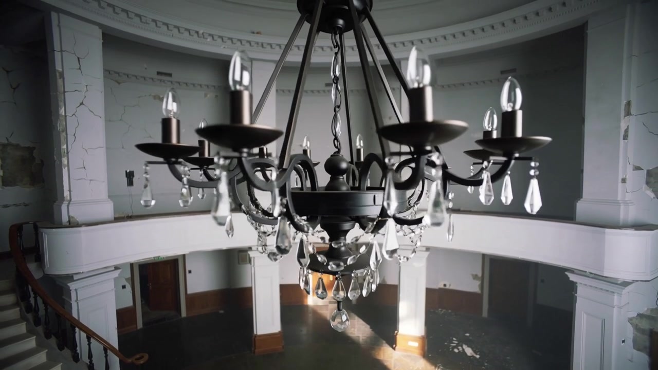 Telecamera che avanza rivelando un lampadario di metallo nell'atrio, mostrando una scalinata ed esponendo il degrado.