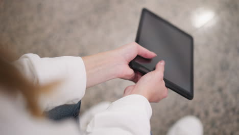 close up of partial view of hands in white sleeve gently holding tablet while seated on granite floor, hands swaying tablet subtly with reflections on screen