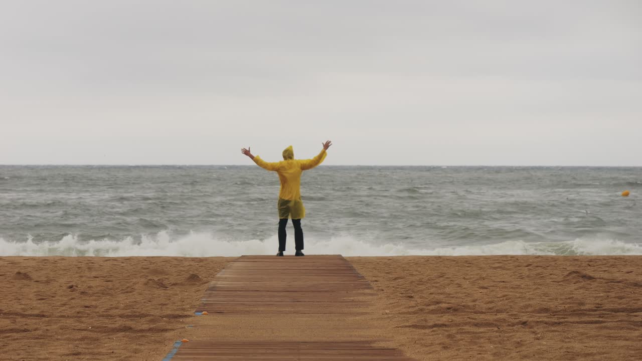 Man tourist person with umbrella and raincoat near sea ocean beach with storm on rainy european city street, lights reflecting, walking in Barcelona or Amsterdam during the rain