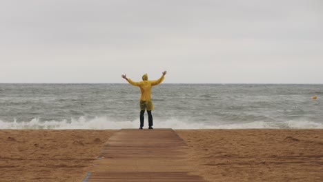 man tourist person with umbrella and raincoat near sea ocean beach with storm on rainy european city street, lights reflecting, walking in barcelona or amsterdam during the rain