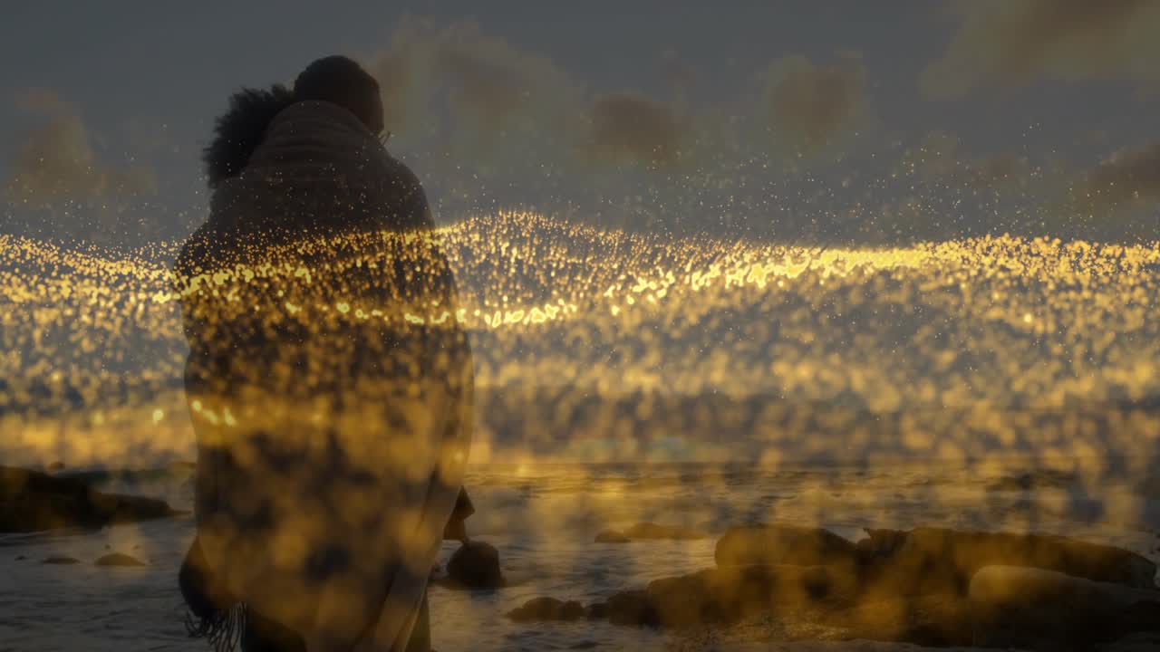 Untersicht zeigt ein sich umarmendes Paar bei Sonnenuntergang für eine Tech-Werbung, goldener Staub umhüllt ihre Silhouetten.