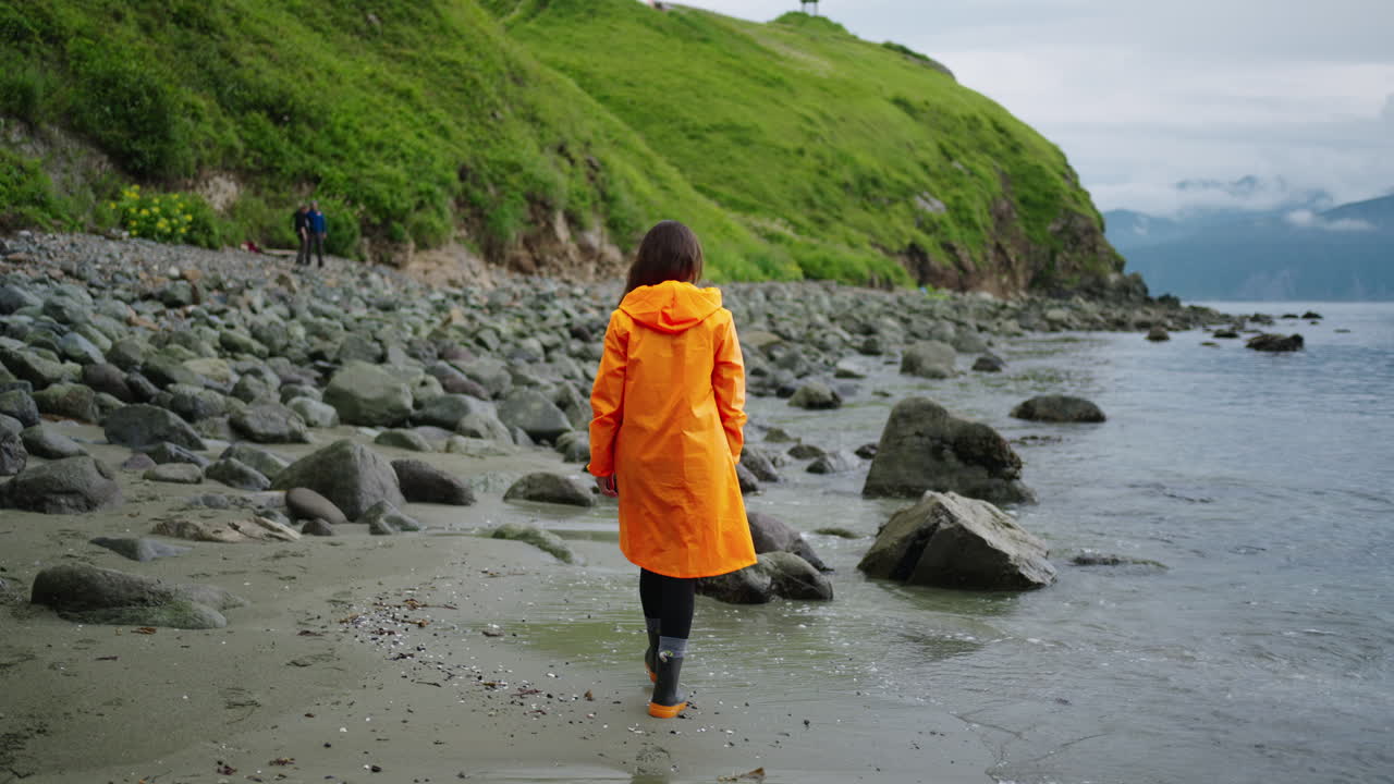Woman walking on a rocky beach in an orange raincoat