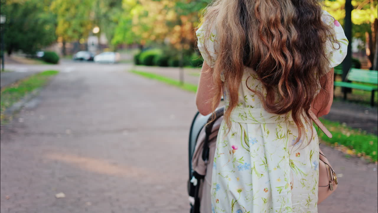 A woman in a floral dress pushing a baby stroller along a park path