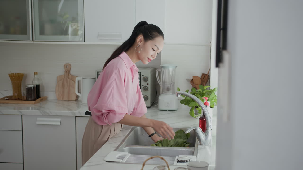 Woman Washing Vegetables and Greenery at Kitchen Sink