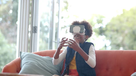 niño afroamericano sentado en el sofá, usando auriculares vr y tocando la pantalla virtual, cámara lenta