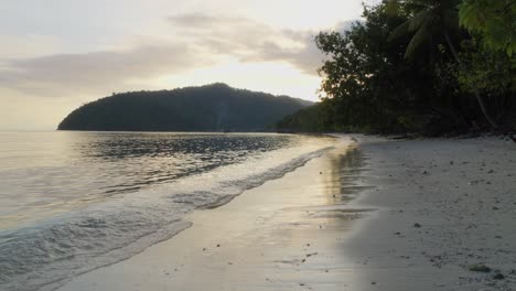 Tranquil-waves-gently-caress-the-sandy-shores-of-Kri-Island-in-the-Raja-Ampat-Archipelago-of-Indonesia,-captured-during-golden-hour-of-sunrise-or-sunset