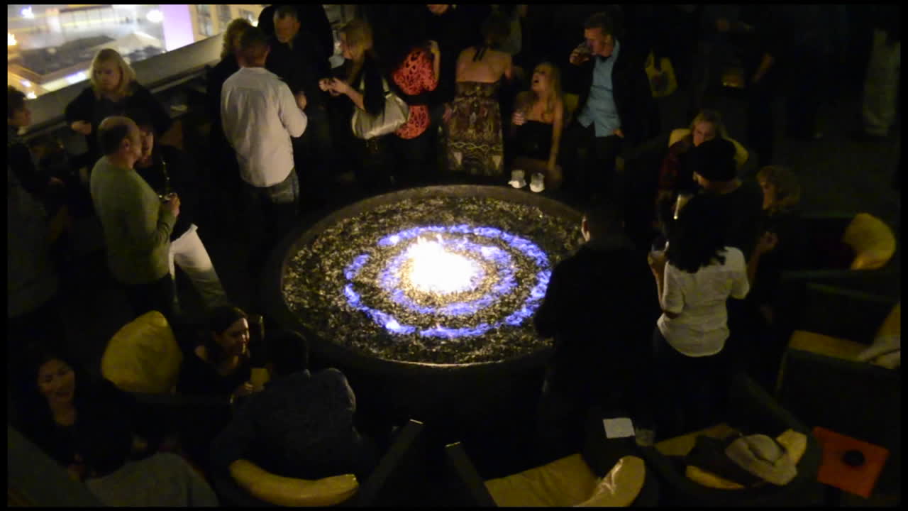Rack focus of adults dancing around a fire at a rooftop nightclub in San Diego California