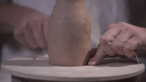male hands are finishing a clay product cutting its bottom with a thread