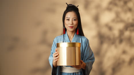 황금 상자를 들고 카메라에 보여주는 파란색 기모노에 젊은 아시아 여자