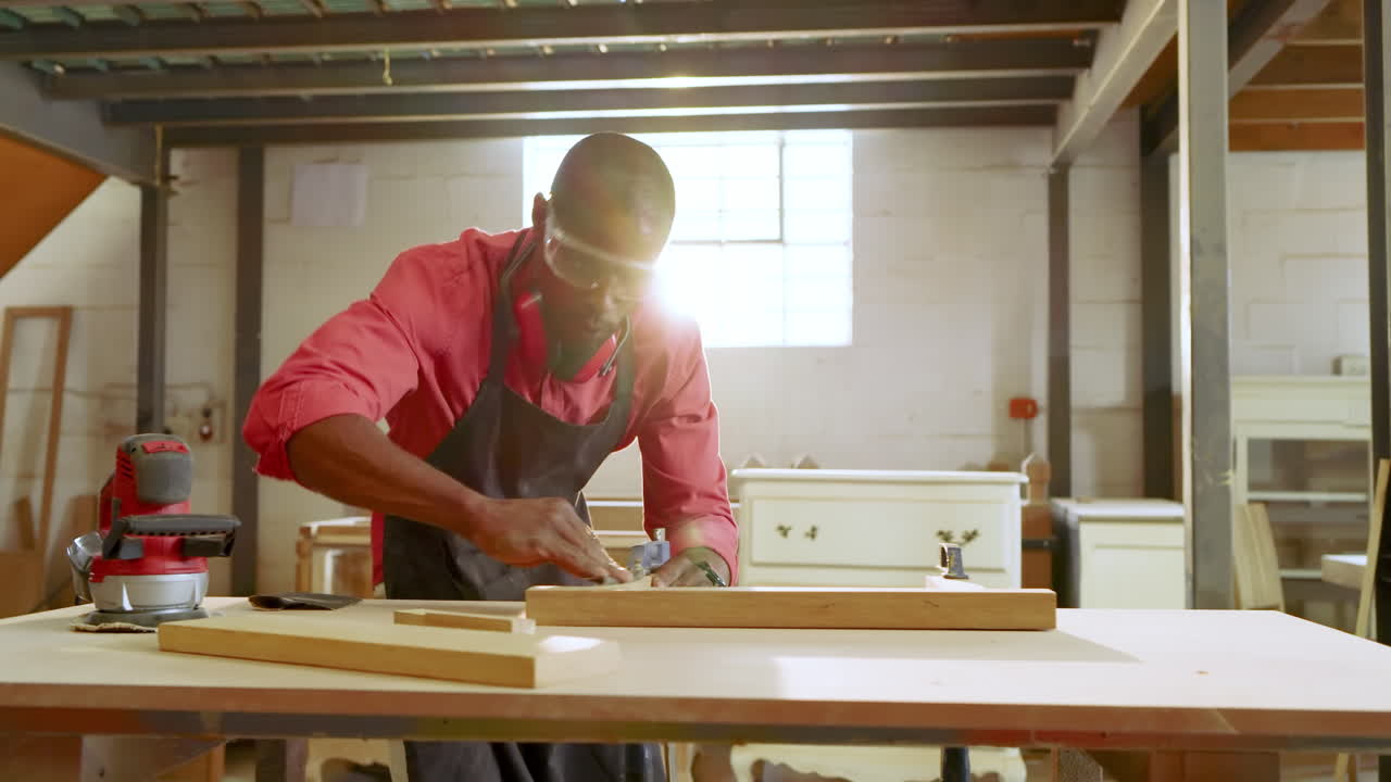 Placing plank against clamp, Black male coworkers sanding wood at workshop and discussing finish