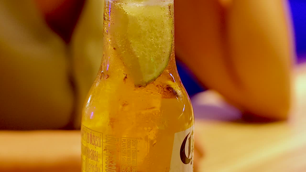 Primo piano estremo di una bottiglia di birra di vetro fredda con una guarnizione di spicchio di lime fresco.