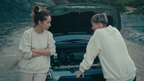 two women facing a broken-down car