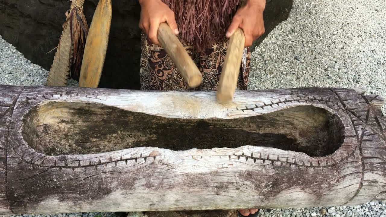 un hombre de la isla del pacífico toca un gran tambor de madera.