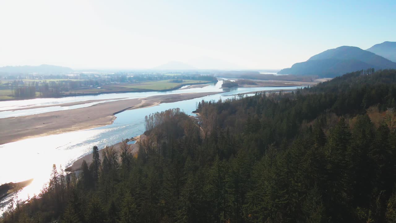 escena cinematográfica sobrevolando bosques de agujas sobre el río fraser en la parte baja del continente en columbia británica en canadá, escena brillante con montañas nubladas en otoño