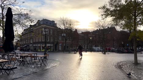 slow motion shot of woman on bicycle riding on street in city of leiden during sunset,netherlands - static wide shot