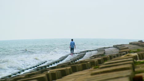 young lonely man walking towards the dangers of incoming ocean tide