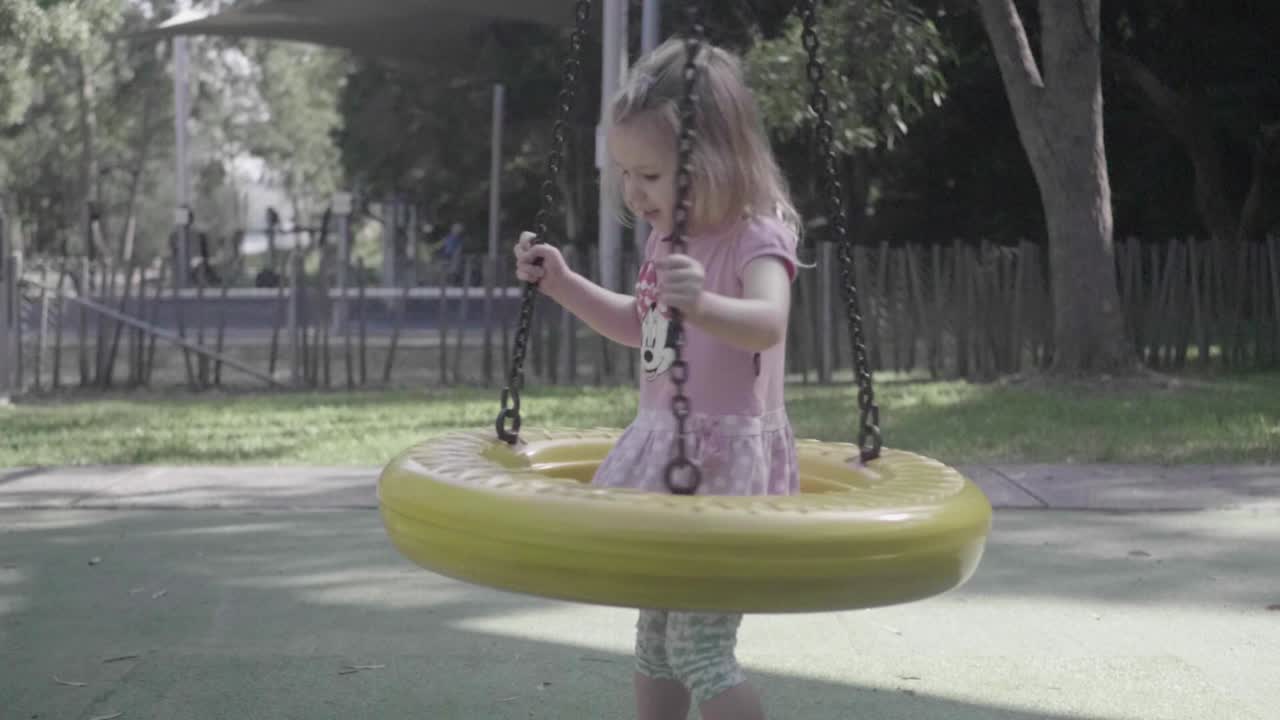 Inquadratura ampia di una bambina di 4 anni che gioca con un'altalena in un parco giochi, ripresa al rallentatore.