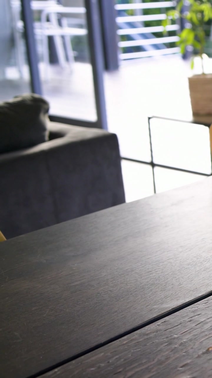 Vertical video: Panning camera showing wooden table filling frame in lounge, exposing laptop, plant
