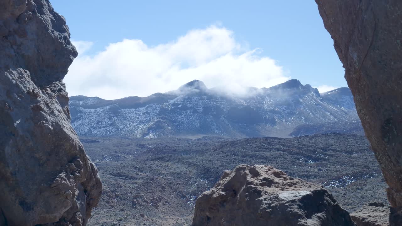 Nuvole che si muovono sopra montagne innevate e un paesaggio roccioso.