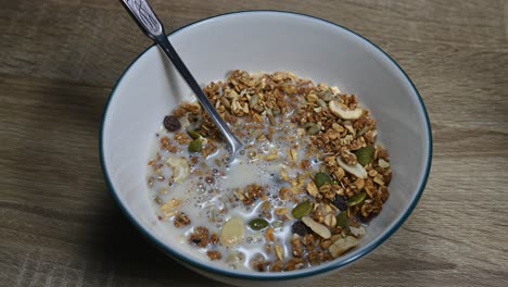 a zoom in of the a bowl of granola and almond milk just poured in making bubbles, seeds, dried fruits, healthy breakfast