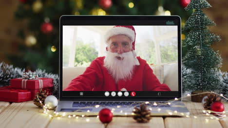 senior caucasian man in santa costume on video call on laptop, with christmas decorations and tree