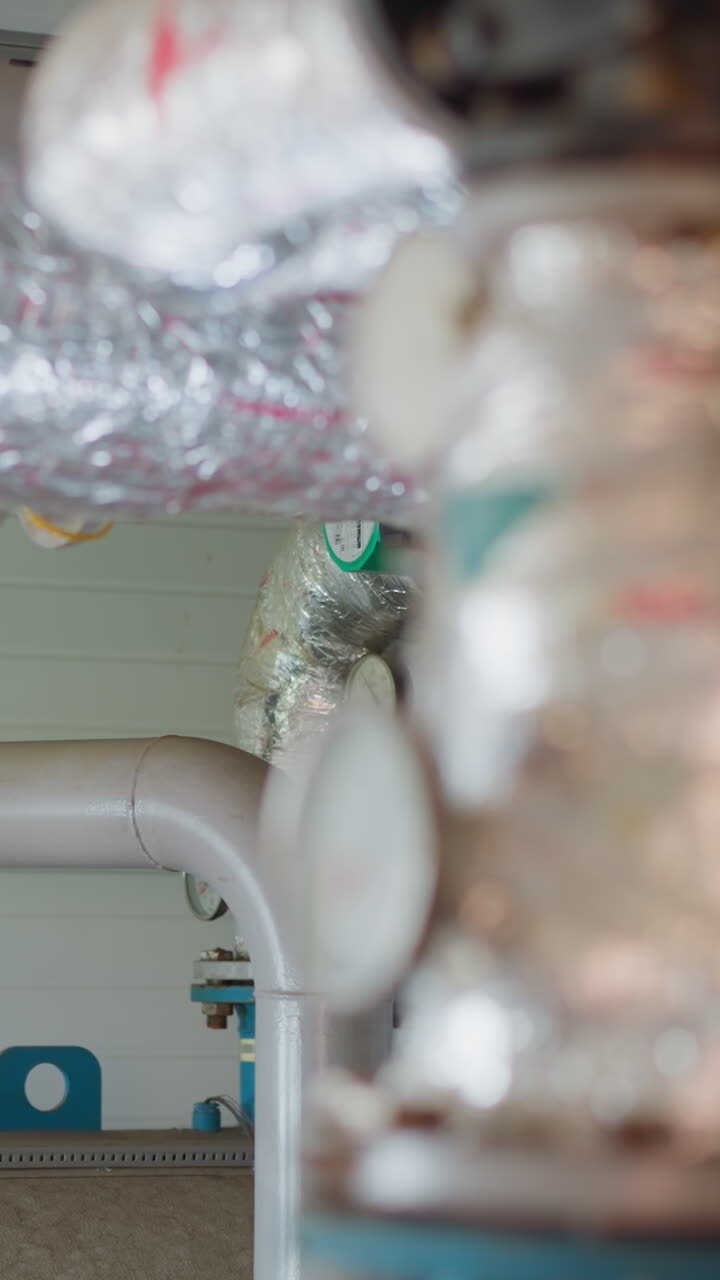 Hot steam flow delivering conduit with silver thermal insulation in mechanical room closeup. Heat transferring system in contemporary building