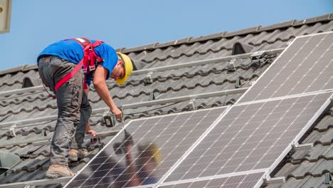 fijación del panel solar a los rieles de montaje en el techo inclinado - trabajador de la construcción caucásico