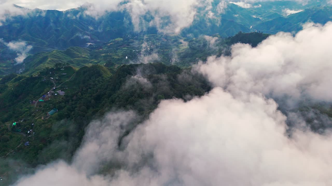 Aerial drone view of thick clouds rolling over lush green mountains and valleys with scattered villages below, perfect for travel, eco projects, documentaries,cinematic storytelling, and inspirational
