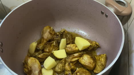 dejando caer papas cortadas en cubitos en una olla de pollo al curry chisporroteante