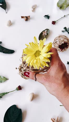 woman's hand holding a yellow flower in a wicker sphere