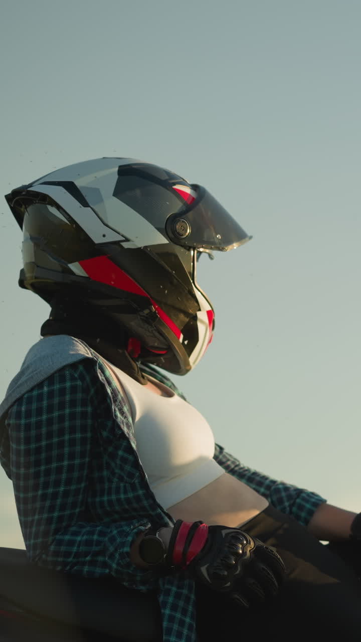 se ve a una motociclista femenina descansando en su bicicleta de potencia roja, con casco y guantes, mientras mira hacia adelante en el campo abierto
