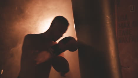 boxeador sin camisa se calienta golpeando el saco de boxeo